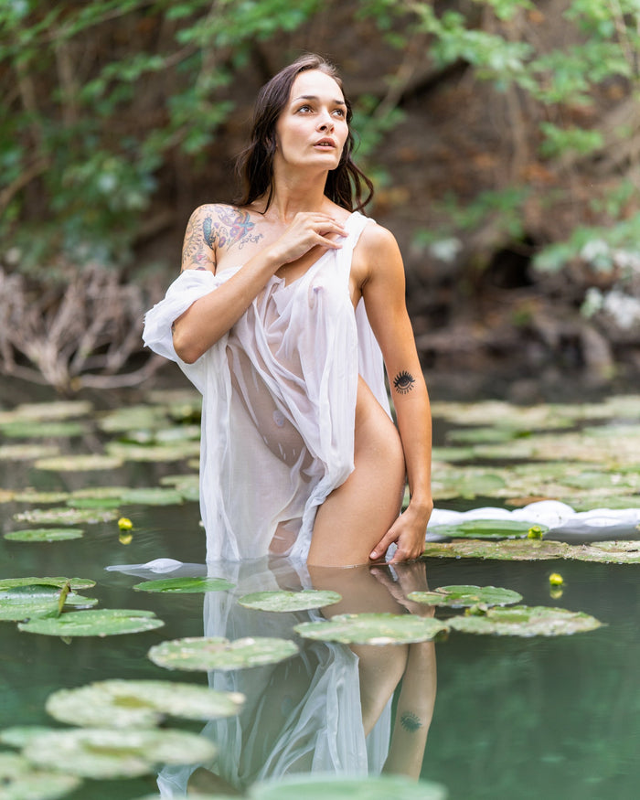 Ayeonna looking up as she stands in a pond wearing a shear white cloth