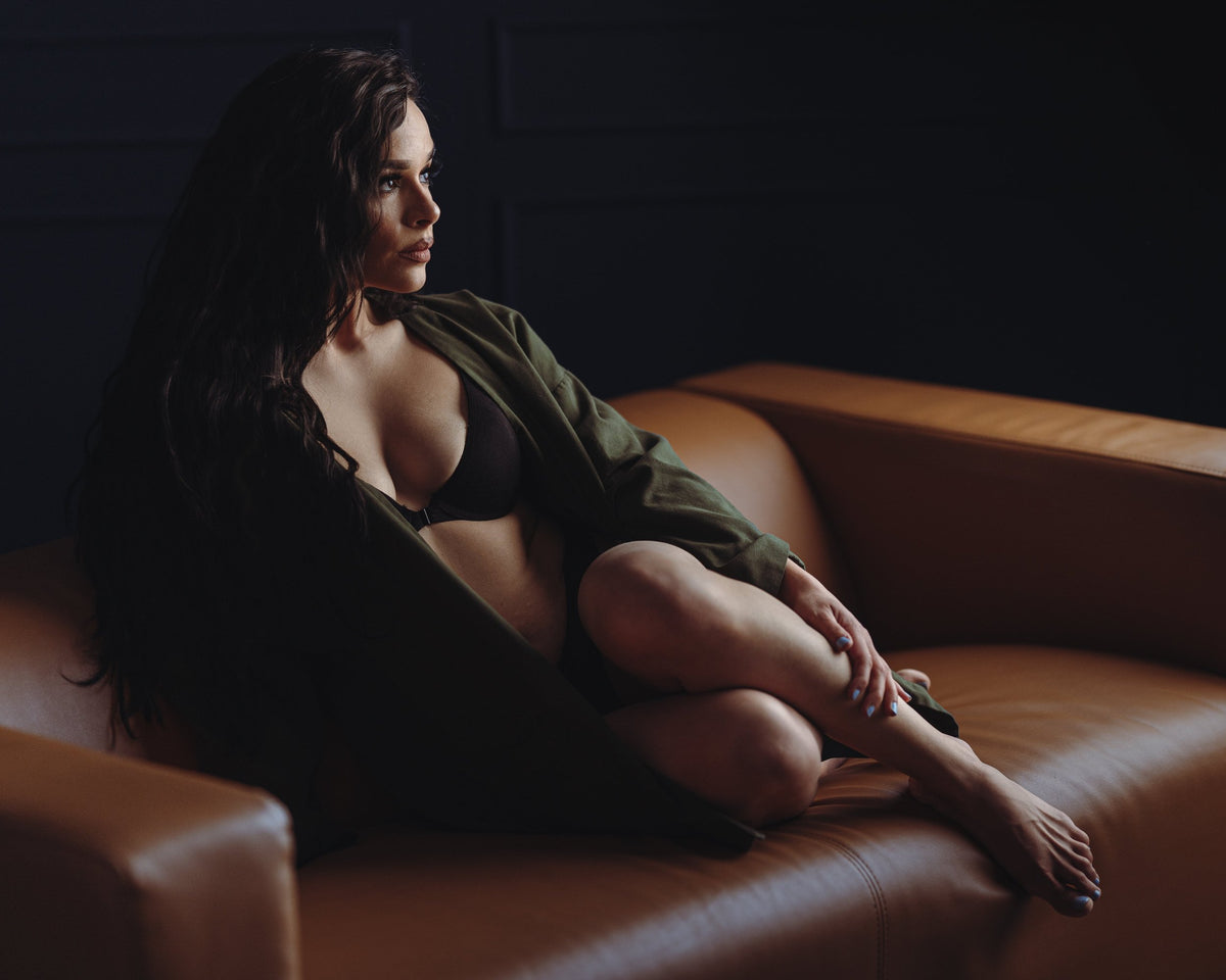 Faith sitting on a leather couch in lingerie with dim soft light